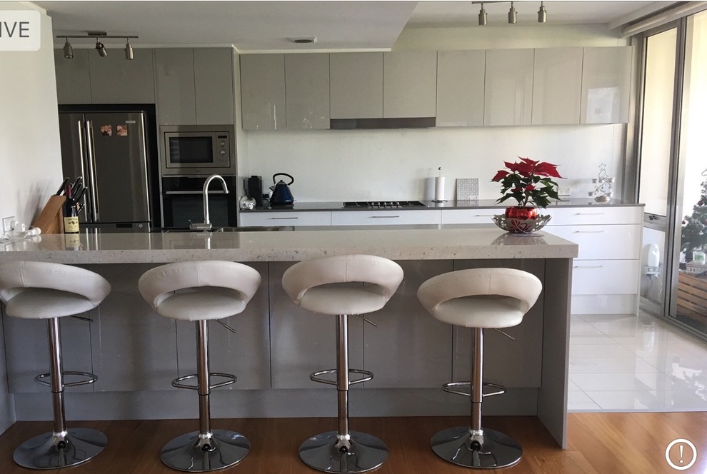 Design ideas for a medium sized contemporary galley kitchen/diner in Wollongong with a double-bowl sink, raised-panel cabinets, grey cabinets, glass worktops, white splashback, glass sheet splashback, stainless steel appliances, ceramic flooring, an island, white floors and grey worktops.