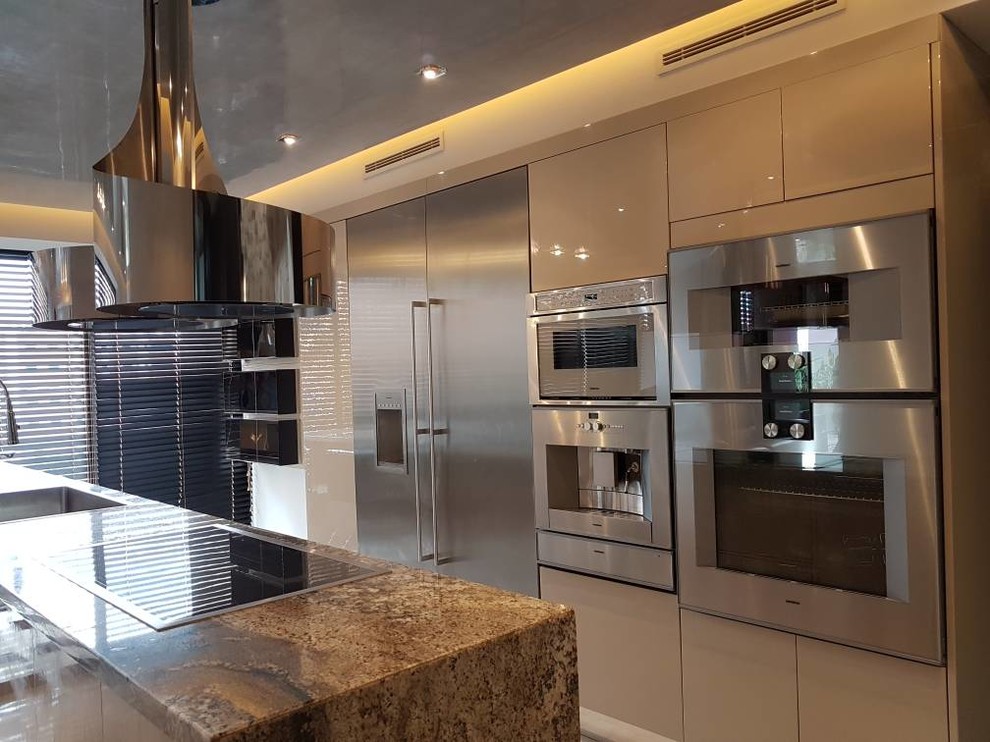 Medium sized modern l-shaped open plan kitchen in Miami with flat-panel cabinets, beige cabinets, granite worktops, an island, a submerged sink, stainless steel appliances, concrete flooring, beige floors and beige worktops.