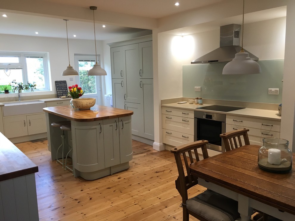 This is an example of a large classic kitchen in Hampshire with a belfast sink, shaker cabinets, blue cabinets, wood worktops, glass sheet splashback, stainless steel appliances, medium hardwood flooring and an island.