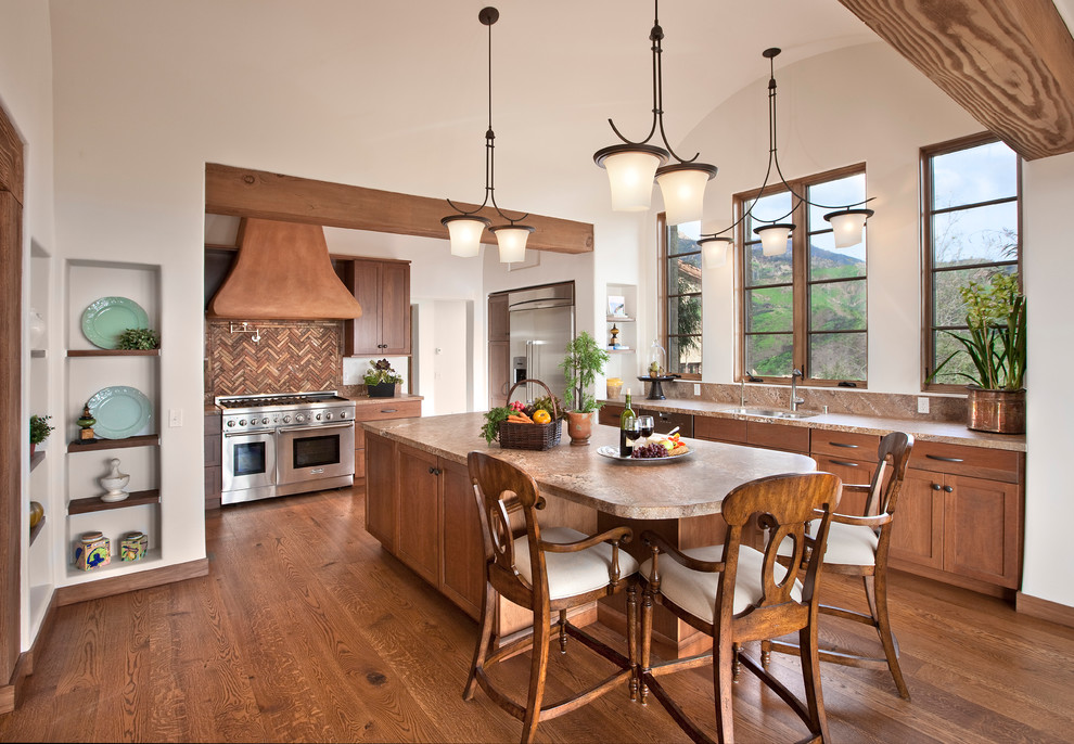 Example of a tuscan medium tone wood floor and brown floor kitchen design in Santa Barbara with an undermount sink, shaker cabinets, medium tone wood cabinets, multicolored backsplash, stainless steel appliances and an island