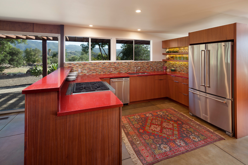 Mid-sized mid-century modern u-shaped concrete floor and gray floor open concept kitchen photo in Santa Barbara with an undermount sink, flat-panel cabinets, medium tone wood cabinets, quartz countertops, multicolored backsplash, glass sheet backsplash, stainless steel appliances and a peninsula