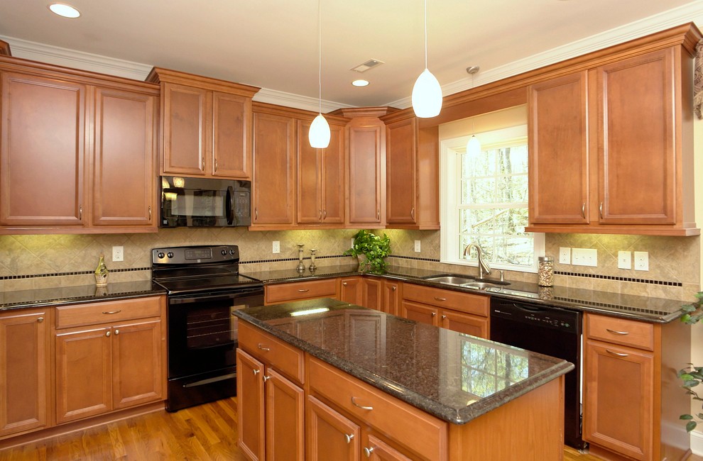 Inspiration for a mid-sized timeless u-shaped light wood floor enclosed kitchen remodel in Raleigh with a double-bowl sink, recessed-panel cabinets, medium tone wood cabinets, granite countertops, black backsplash, ceramic backsplash, black appliances and an island
