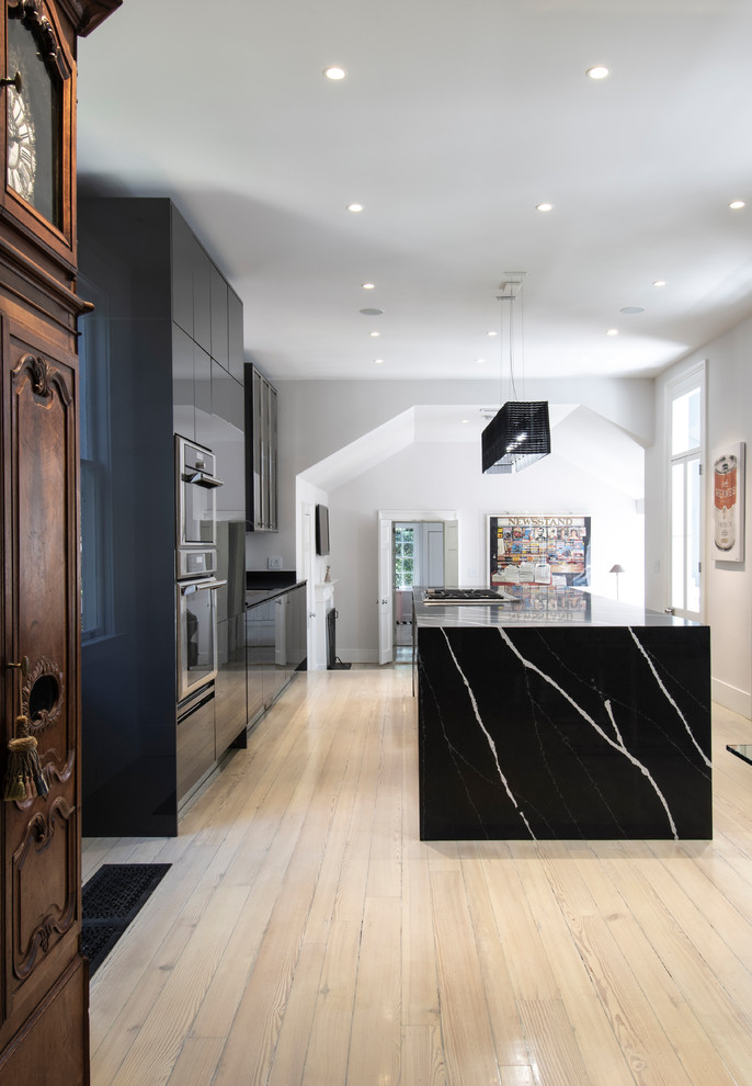Inspiration för ett stort funkis svart svart kök, med en undermonterad diskho, släta luckor, svarta skåp, bänkskiva i kvarts, stänkskydd med metallisk yta, stänkskydd i metallkakel, integrerade vitvaror, ljust trägolv och en köksö