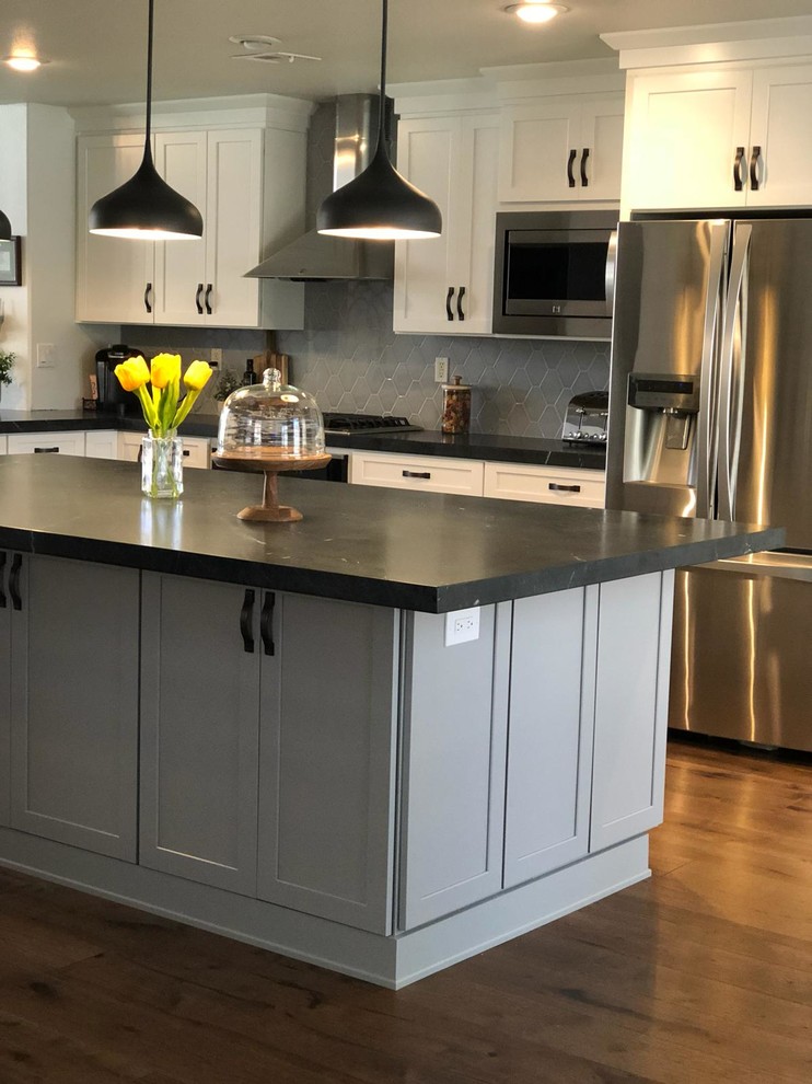 Medium sized traditional l-shaped kitchen/diner in Las Vegas with a built-in sink, shaker cabinets, white cabinets, engineered stone countertops, grey splashback, ceramic splashback, stainless steel appliances, medium hardwood flooring, an island, brown floors and black worktops.
