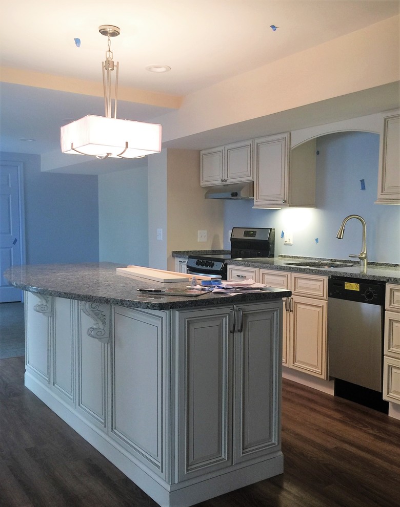 Bild på ett mellanstort funkis kök, med en undermonterad diskho, luckor med upphöjd panel, vita skåp, granitbänkskiva, blått stänkskydd, rostfria vitvaror, mellanmörkt trägolv, en köksö och brunt golv