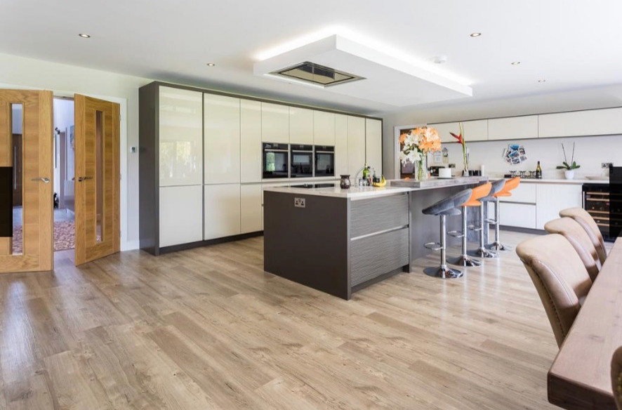 Foto på ett funkis grå kök, med släta luckor, beige skåp, bänkskiva i kvarts, mellanmörkt trägolv, en köksö och beiget golv