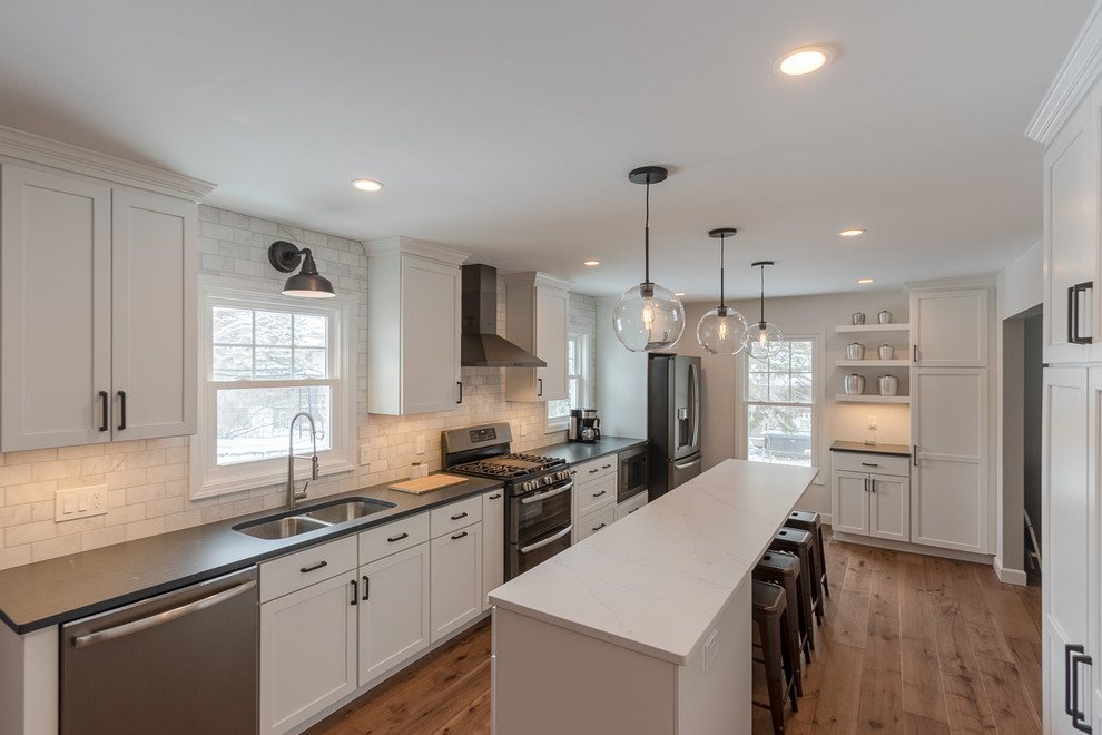 Photo of a large contemporary u-shaped kitchen/diner in Grand Rapids with a double-bowl sink, shaker cabinets, white cabinets, marble worktops, white splashback, marble splashback, stainless steel appliances, medium hardwood flooring, an island, brown floors and white worktops.