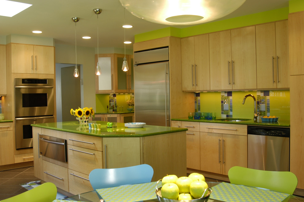 This is an example of a medium sized bohemian l-shaped kitchen/diner in New York with glass tiled splashback, stainless steel appliances, green splashback, flat-panel cabinets, light wood cabinets, a submerged sink, engineered stone countertops, ceramic flooring, an island and green worktops.