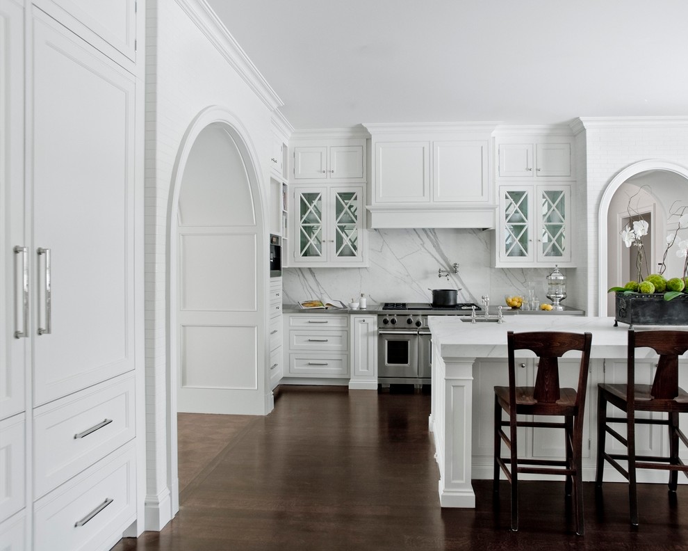 Cette image montre une cuisine traditionnelle avec un placard à porte vitrée, des portes de placard blanches, une crédence blanche, un électroménager en acier inoxydable et une crédence en marbre.