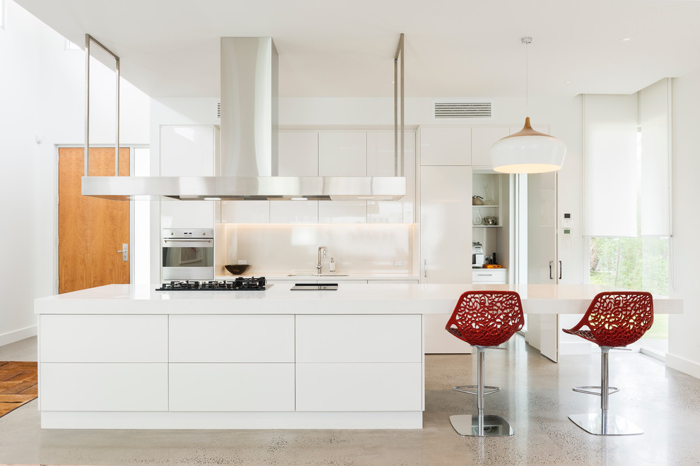 Стильный дизайн: параллельная кухня в современном стиле с двойной мойкой, плоскими фасадами, белыми фасадами, белым фартуком, техникой из нержавеющей стали, бетонным полом и островом - последний тренд