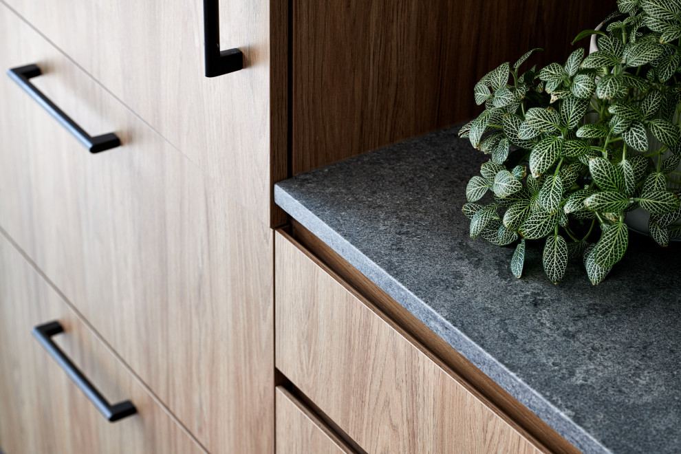 Foto på ett mellanstort nordiskt grå kök, med en undermonterad diskho, släta luckor, skåp i mellenmörkt trä, bänkskiva i kvarts, grått stänkskydd, svarta vitvaror, mörkt trägolv, en köksö och brunt golv