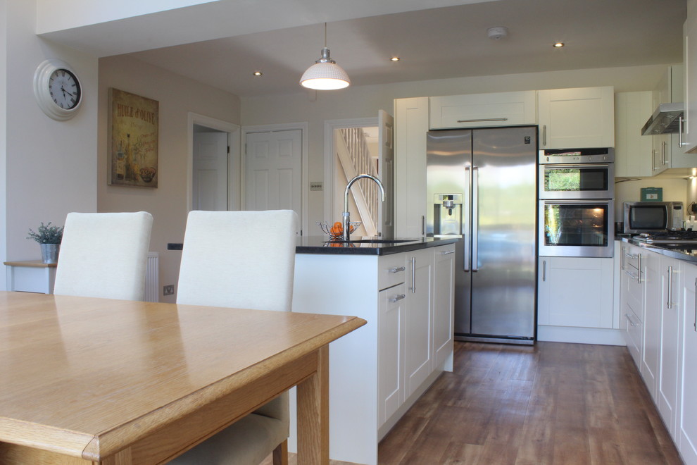 This is an example of a medium sized farmhouse l-shaped kitchen/diner in Hertfordshire with a submerged sink, shaker cabinets, beige cabinets, granite worktops, stainless steel appliances and an island.