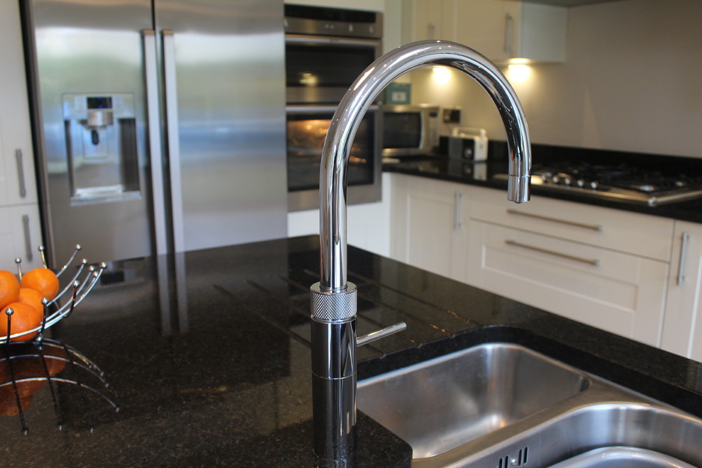 This is an example of a medium sized rural l-shaped kitchen/diner in Hertfordshire with a submerged sink, shaker cabinets, beige cabinets, granite worktops, stainless steel appliances and an island.