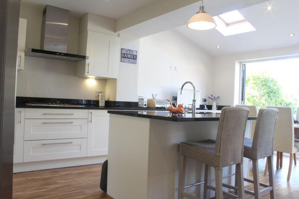 This is an example of a medium sized rural l-shaped kitchen/diner in Hertfordshire with a submerged sink, shaker cabinets, beige cabinets, granite worktops, stainless steel appliances and an island.
