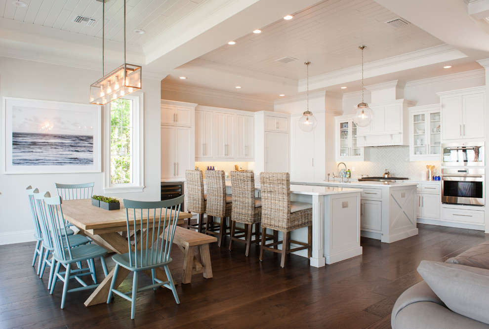 Photo of a coastal open plan kitchen in Orlando with shaker cabinets, white cabinets, white splashback, stainless steel appliances, dark hardwood flooring, multiple islands, brown floors and white worktops.