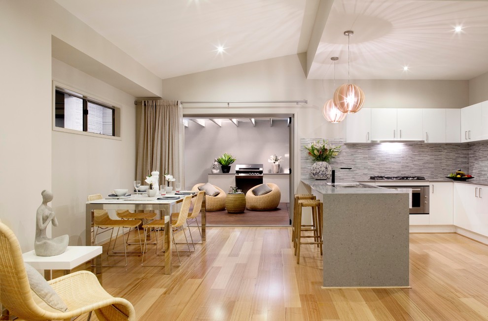 На фото: п-образная кухня-гостиная в современном стиле с плоскими фасадами, белыми фасадами и серым фартуком с