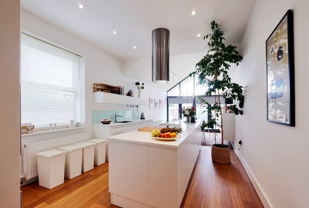 Bild på ett mellanstort funkis kök och matrum, med en dubbel diskho, släta luckor, vita skåp, grönt stänkskydd, glaspanel som stänkskydd, rostfria vitvaror, bambugolv, en köksö, bänkskiva i täljsten och brunt golv