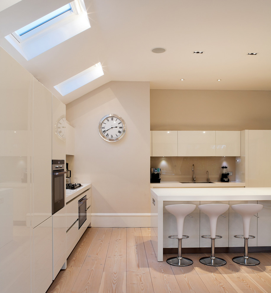 Moderne Küche in L-Form mit flächenbündigen Schrankfronten, weißen Schränken, braunem Holzboden und Kücheninsel in London