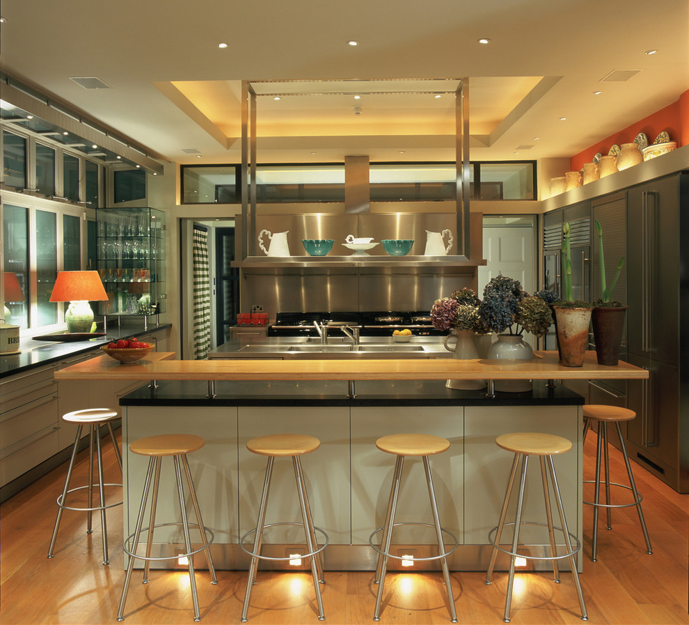 На фото: п-образная кухня в современном стиле с плоскими фасадами, серыми фасадами, фартуком цвета металлик, паркетным полом среднего тона и островом с