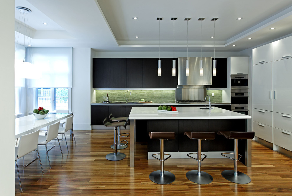 Modern inredning av ett stort linjärt kök och matrum, med rostfria vitvaror, en undermonterad diskho, släta luckor, svarta skåp, bänkskiva i koppar, grönt stänkskydd, stänkskydd i stickkakel, en köksö och mörkt trägolv