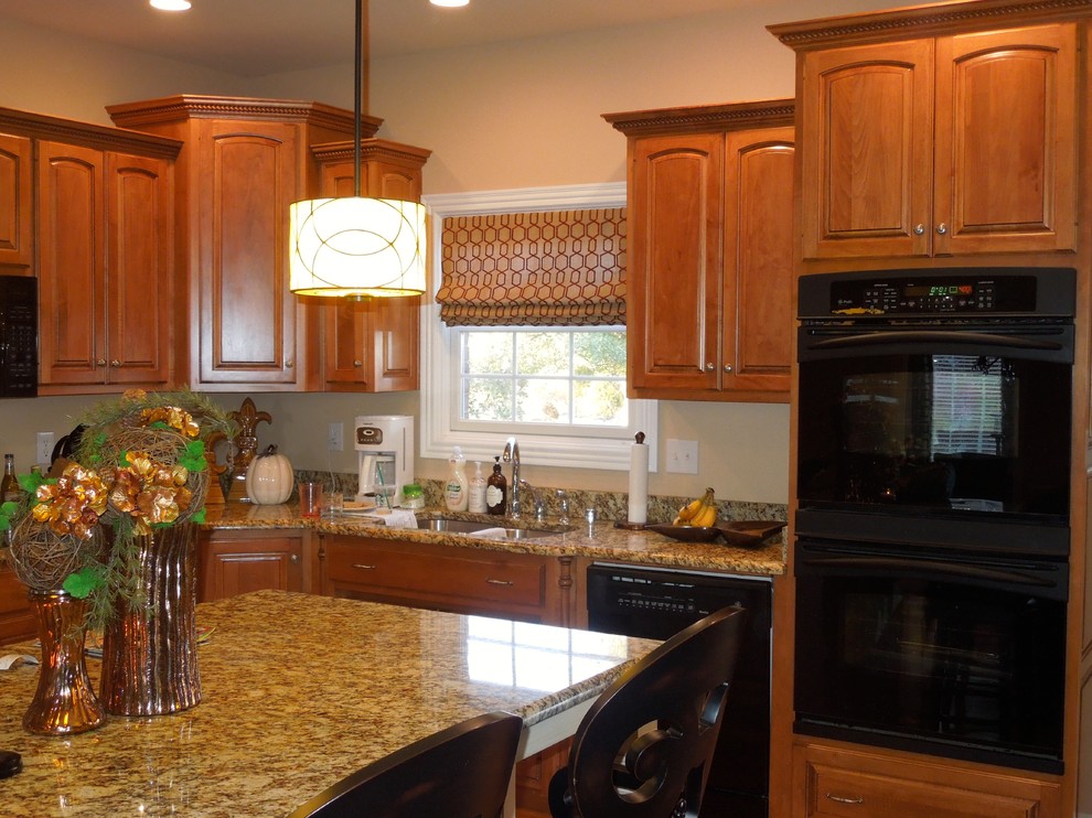 Klassische Wohnküche mit hellbraunen Holzschränken, Granit-Arbeitsplatte, schwarzen Elektrogeräten und Kücheninsel in Louisville