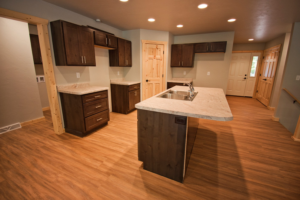 This is an example of a medium sized rustic l-shaped kitchen/diner in Other with a double-bowl sink, recessed-panel cabinets, dark wood cabinets, medium hardwood flooring, an island, brown floors and grey worktops.
