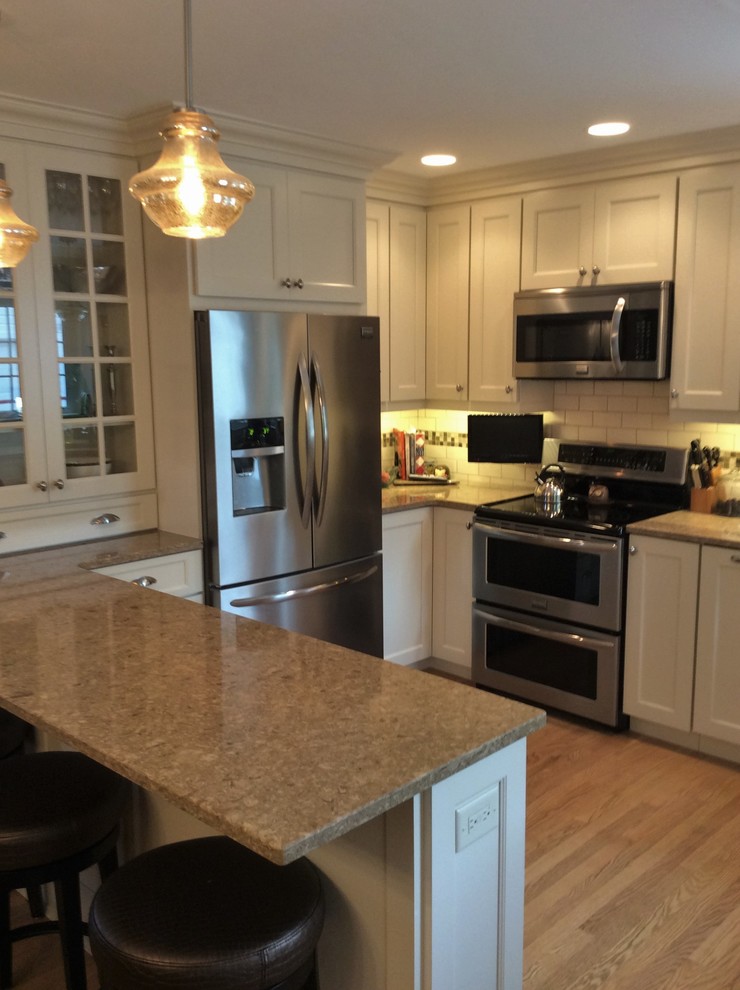 Mid-sized elegant u-shaped light wood floor eat-in kitchen photo in Chicago with shaker cabinets, white cabinets, quartz countertops, white backsplash, subway tile backsplash, stainless steel appliances, a peninsula and an undermount sink