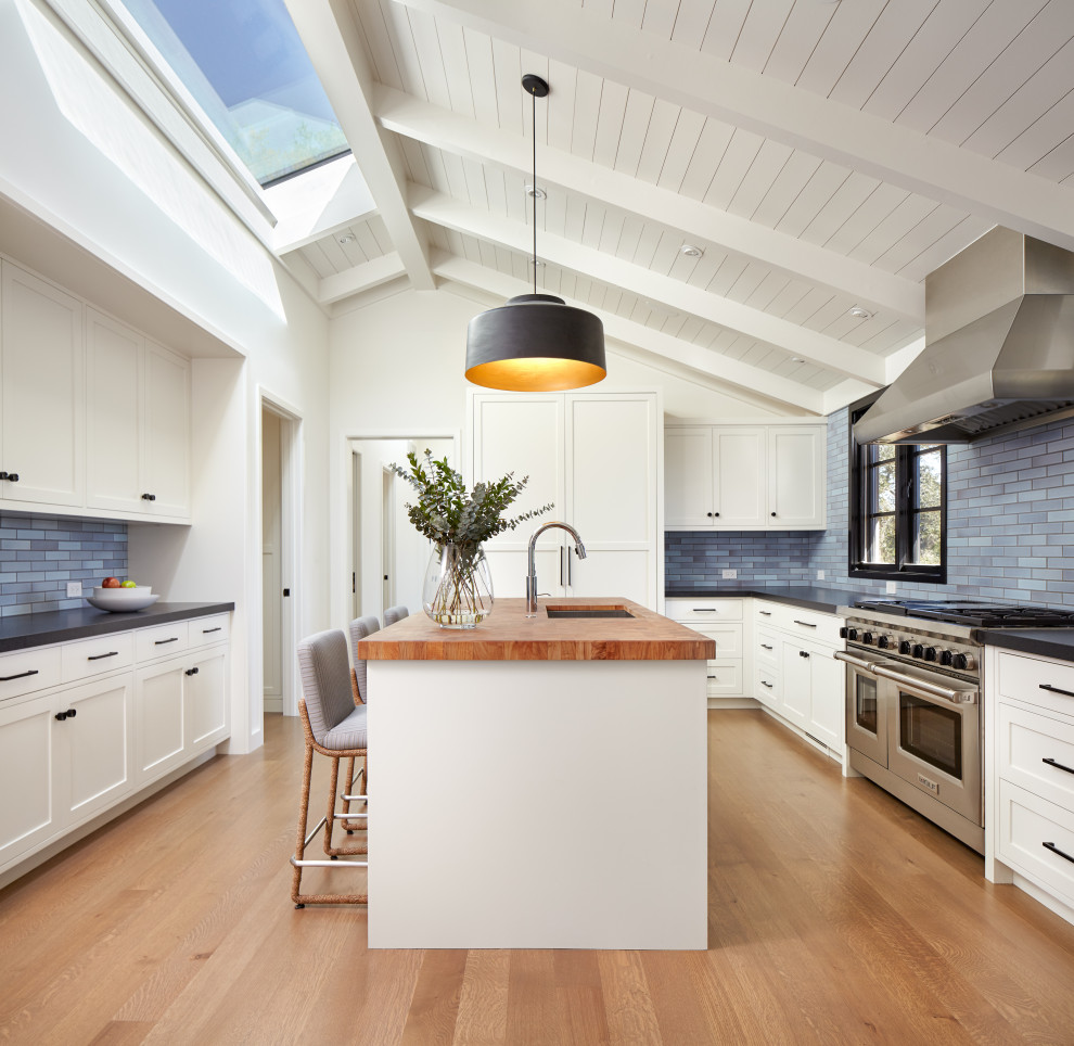 Inspiration for a transitional u-shaped medium tone wood floor, brown floor and shiplap ceiling enclosed kitchen remodel in San Francisco with an undermount sink, shaker cabinets, white cabinets, wood countertops, blue backsplash, subway tile backsplash, paneled appliances, an island and brown countertops