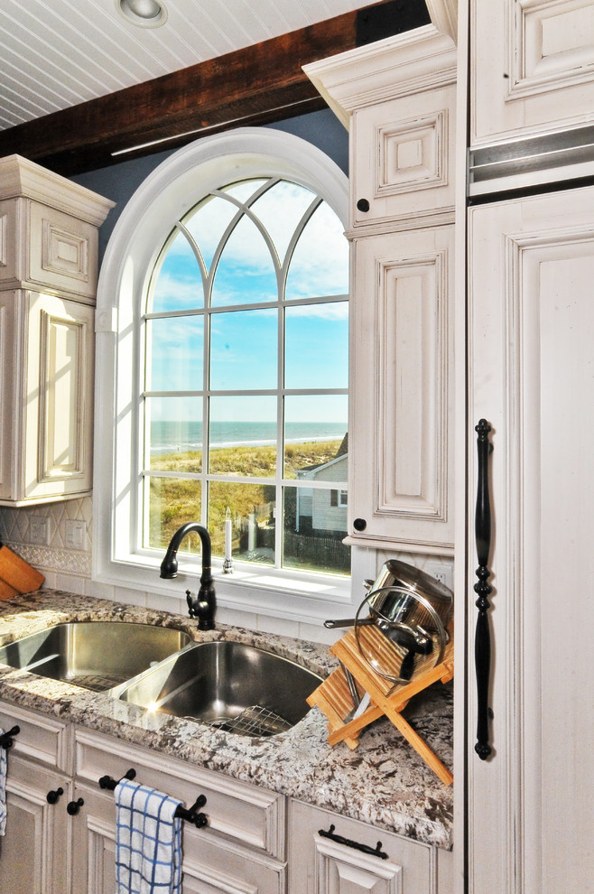 Medelhavsstil inredning av ett kök, med en dubbel diskho, granitbänkskiva, luckor med upphöjd panel, vita skåp och integrerade vitvaror