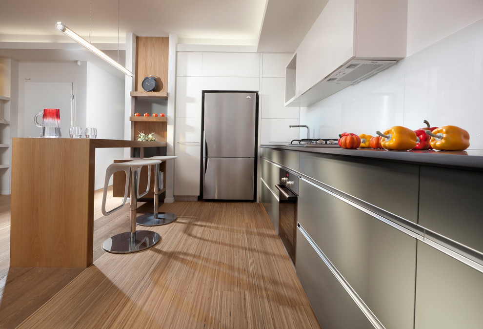 Immagine di una cucina moderna con elettrodomestici in acciaio inossidabile, ante lisce, ante grigie, paraspruzzi bianco e paraspruzzi con lastra di vetro
