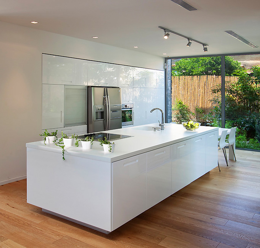 Cette photo montre une cuisine parallèle moderne avec un électroménager en acier inoxydable, un évier intégré, un placard à porte plane et des portes de placard blanches.