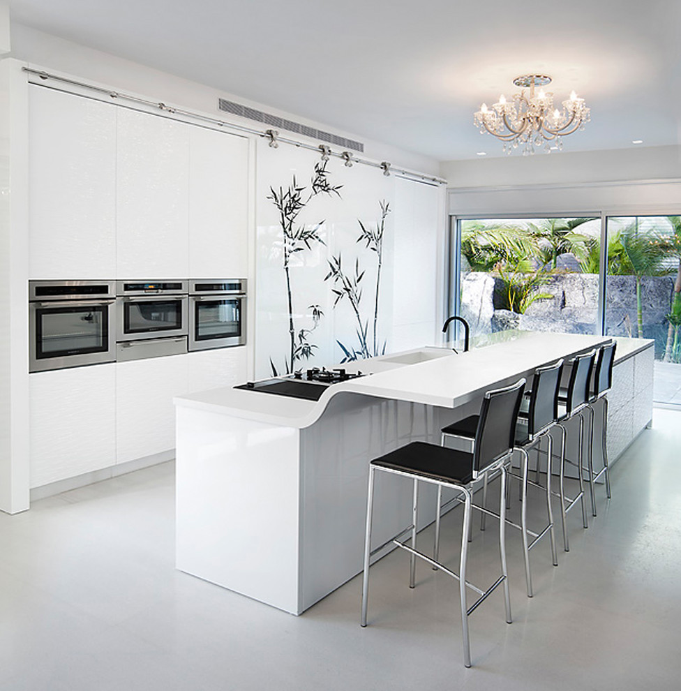 Trendy galley kitchen photo in Other with stainless steel appliances, an integrated sink, white cabinets and solid surface countertops