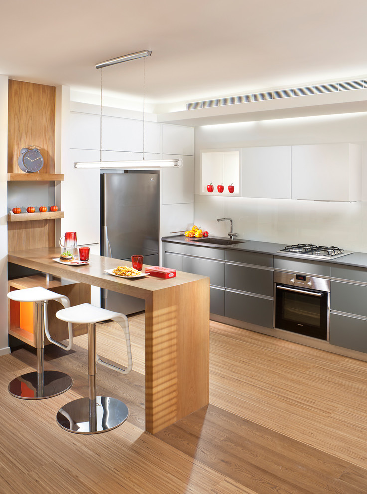 Moderne Küchenbar in L-Form mit flächenbündigen Schrankfronten, grauen Schränken, Arbeitsplatte aus Holz, Küchenrückwand in Weiß, Glasrückwand und Küchengeräten aus Edelstahl in Sonstige