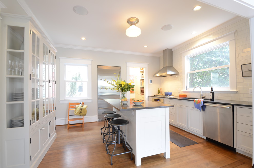 Modern inredning av ett kök, med stänkskydd i tunnelbanekakel, luckor med glaspanel, vita skåp, rostfria vitvaror, vitt stänkskydd och en undermonterad diskho