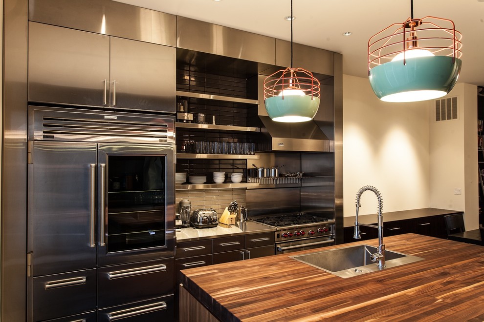 Eat-in kitchen - mid-sized contemporary single-wall dark wood floor and brown floor eat-in kitchen idea in Chicago with stainless steel cabinets, an island, flat-panel cabinets, wood countertops, gray backsplash, stainless steel appliances, an undermount sink and glass tile backsplash