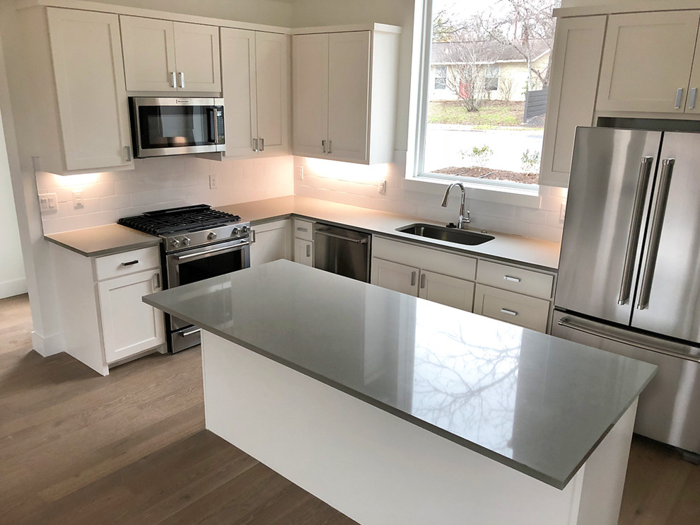 Mid-sized minimalist u-shaped medium tone wood floor and brown floor open concept kitchen photo in Austin with an undermount sink, shaker cabinets, white cabinets, quartz countertops, white backsplash, subway tile backsplash, stainless steel appliances, an island and gray countertops