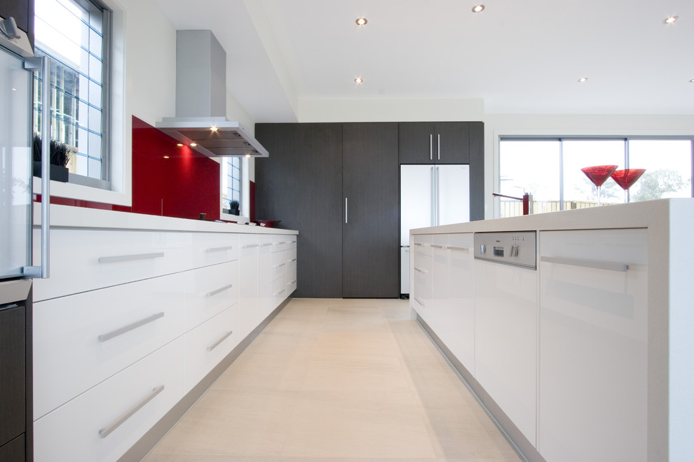 Idée de décoration pour une cuisine parallèle minimaliste avec un placard à porte plane, des portes de placard blanches, une crédence rouge, une crédence en feuille de verre et un électroménager blanc.