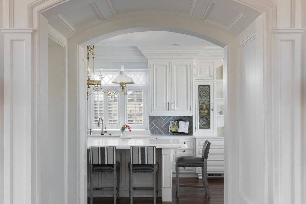 Inspiration for a huge transitional u-shaped medium tone wood floor and brown floor open concept kitchen remodel in Newark with a farmhouse sink, raised-panel cabinets, white cabinets, quartz countertops, gray backsplash, ceramic backsplash, white appliances, an island and white countertops