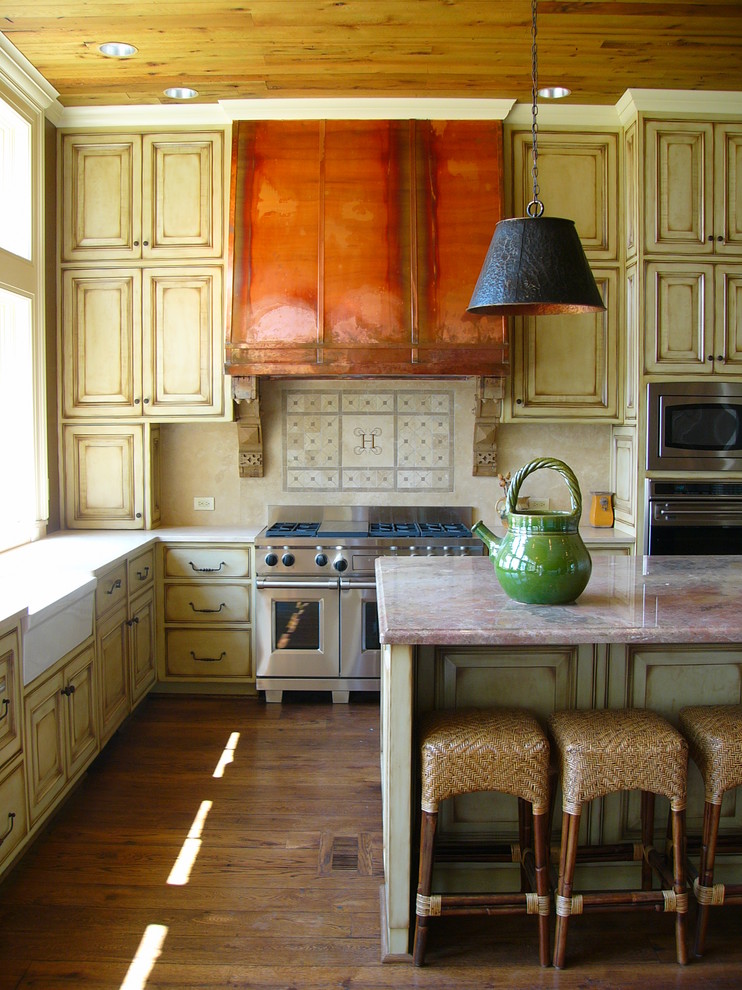 Bild på ett vintage kök, med rostfria vitvaror, en rustik diskho, luckor med upphöjd panel, skåp i slitet trä, marmorbänkskiva och beige stänkskydd