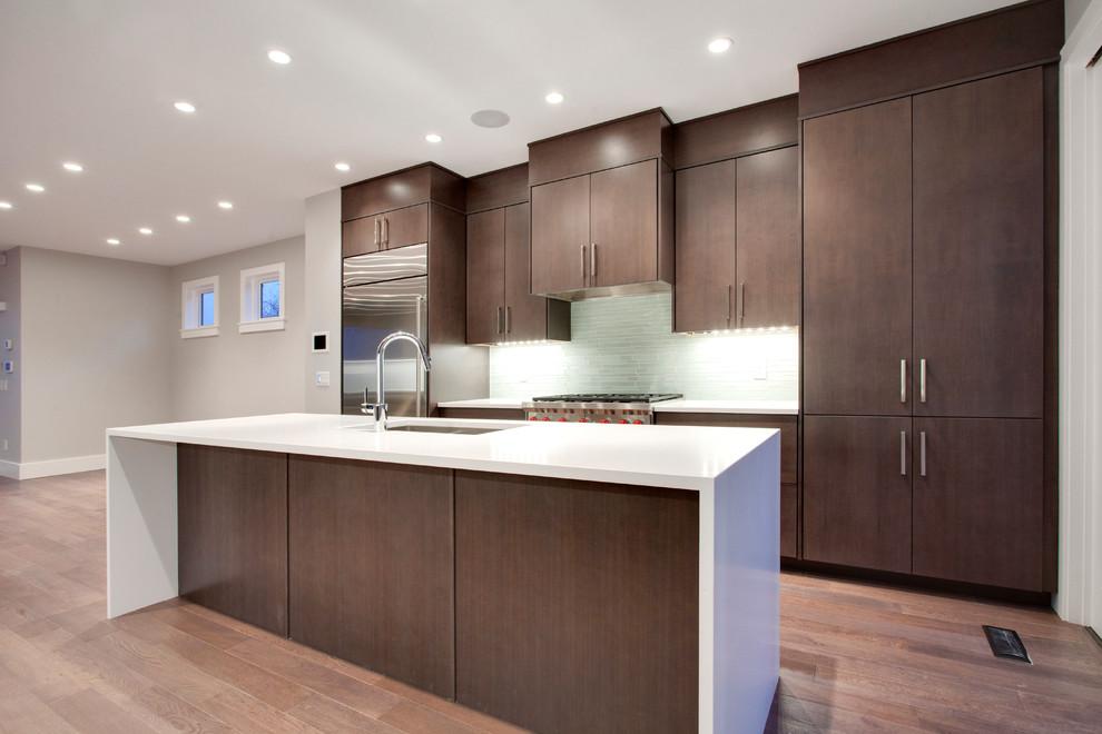This is an example of a small modern galley kitchen/diner in Calgary with a submerged sink, flat-panel cabinets, dark wood cabinets, quartz worktops, white splashback, glass tiled splashback, stainless steel appliances, medium hardwood flooring and an island.