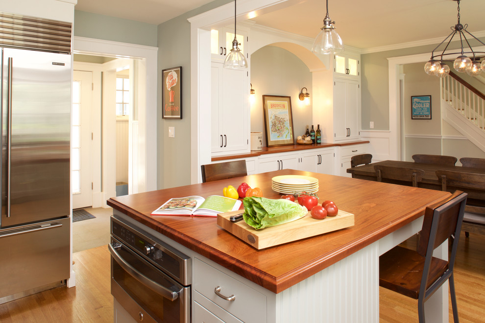 Inredning av ett klassiskt mellanstort kök, med en undermonterad diskho, luckor med infälld panel, vita skåp, träbänkskiva, grönt stänkskydd, stänkskydd i keramik, rostfria vitvaror, mellanmörkt trägolv och en köksö