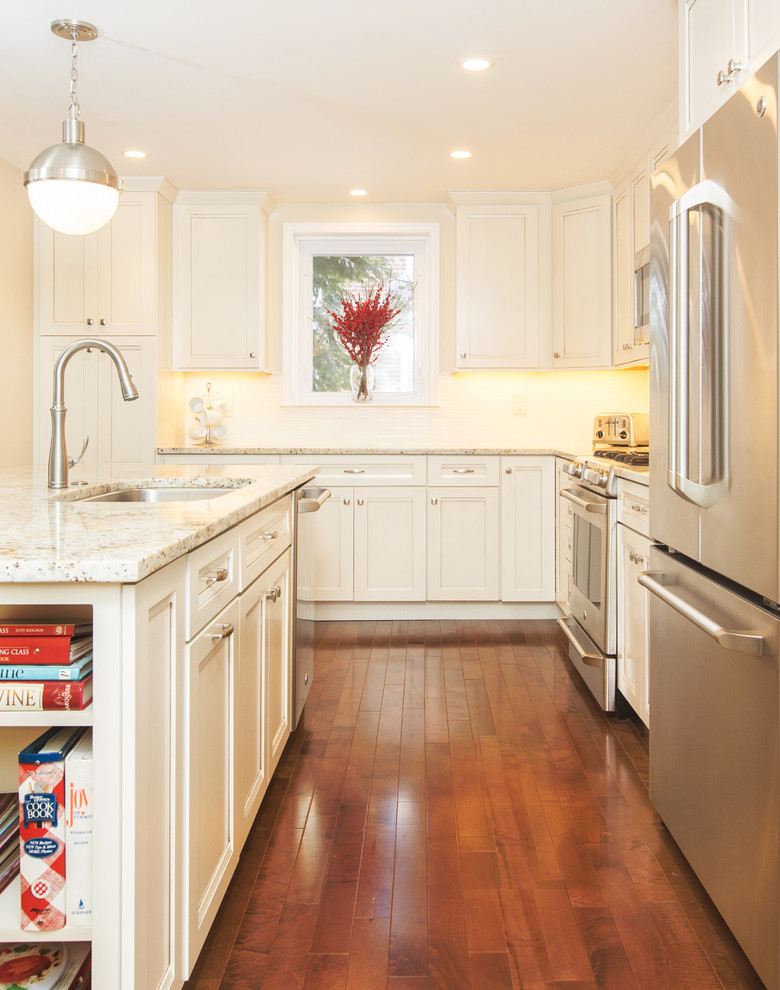 Example of a mid-sized transitional l-shaped medium tone wood floor open concept kitchen design in Philadelphia with an undermount sink, recessed-panel cabinets, white cabinets, granite countertops, white backsplash, ceramic backsplash, stainless steel appliances and an island