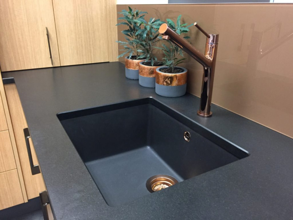 Photo of a contemporary l-shaped kitchen in Christchurch with a submerged sink, granite worktops, glass sheet splashback and black floors.