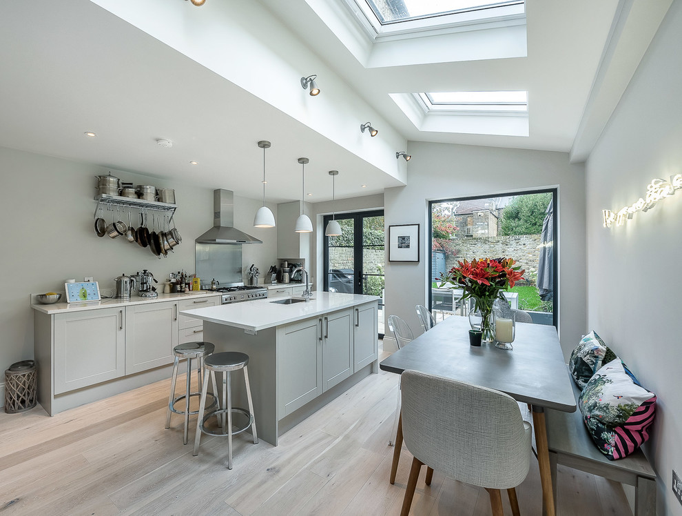 Example of a transitional galley light wood floor eat-in kitchen design in London with an undermount sink, shaker cabinets, gray cabinets and an island