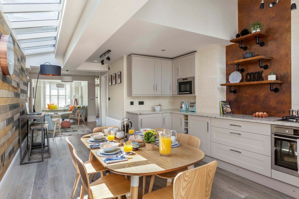Photo of a classic l-shaped open plan kitchen in Kent with shaker cabinets, grey cabinets, white splashback, metro tiled splashback, stainless steel appliances and light hardwood flooring.