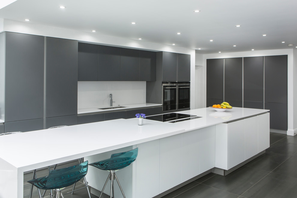 Large contemporary single-wall open plan kitchen in Essex with an integrated sink, flat-panel cabinets, grey cabinets, quartz worktops, white splashback, stone slab splashback, stainless steel appliances, porcelain flooring and an island.