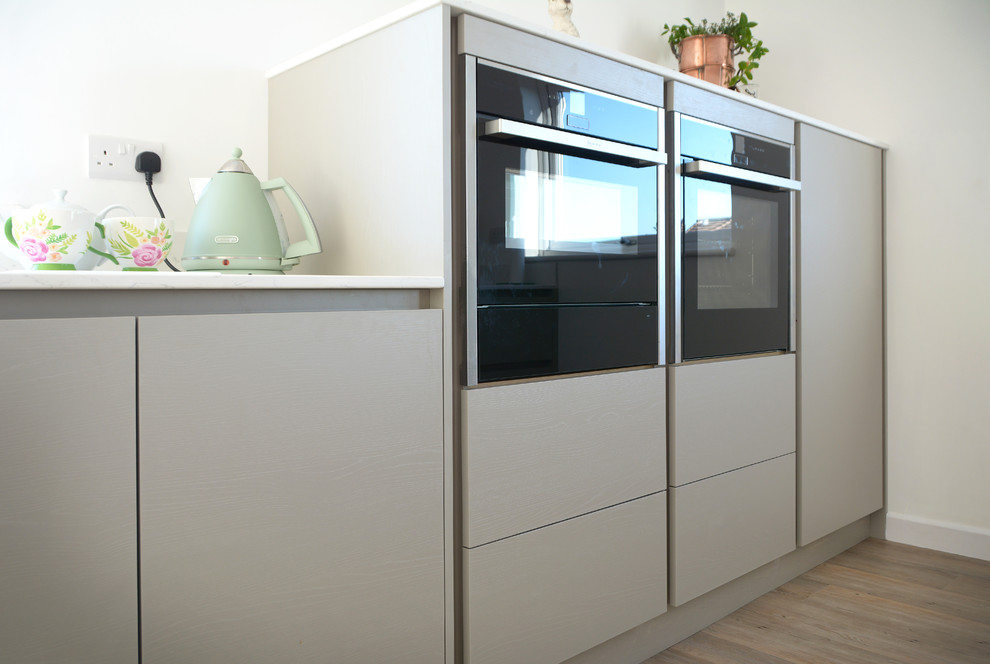 Esempio di una cucina minimalista di medie dimensioni con lavello da incasso, ante lisce, top in superficie solida, paraspruzzi bianco, elettrodomestici neri, pavimento marrone e top bianco