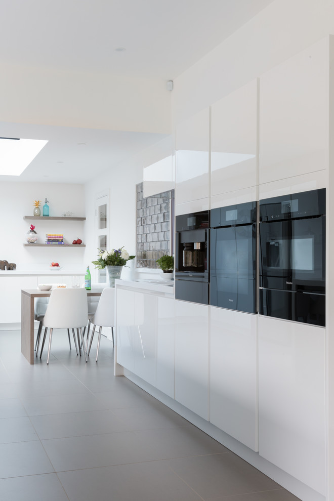 Medium sized contemporary kitchen/diner in West Midlands with flat-panel cabinets, white cabinets, black appliances, ceramic flooring, an island and grey floors.