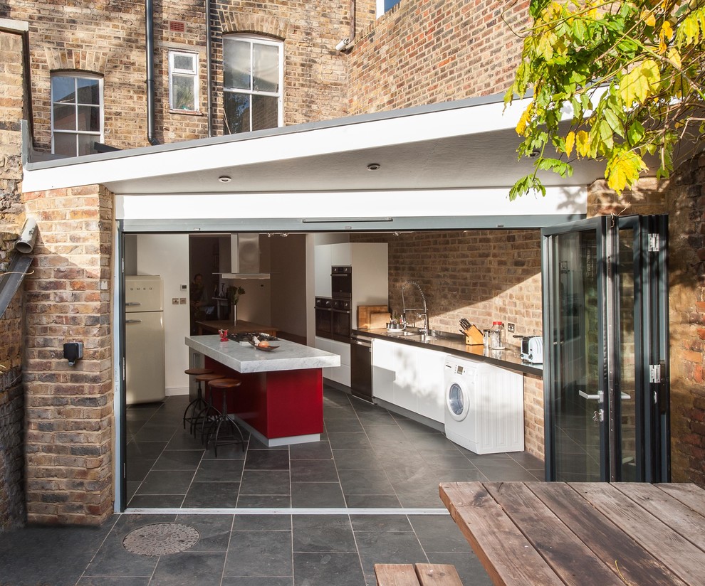 Example of a small trendy slate floor and gray floor enclosed kitchen design in London with flat-panel cabinets, white cabinets and an island