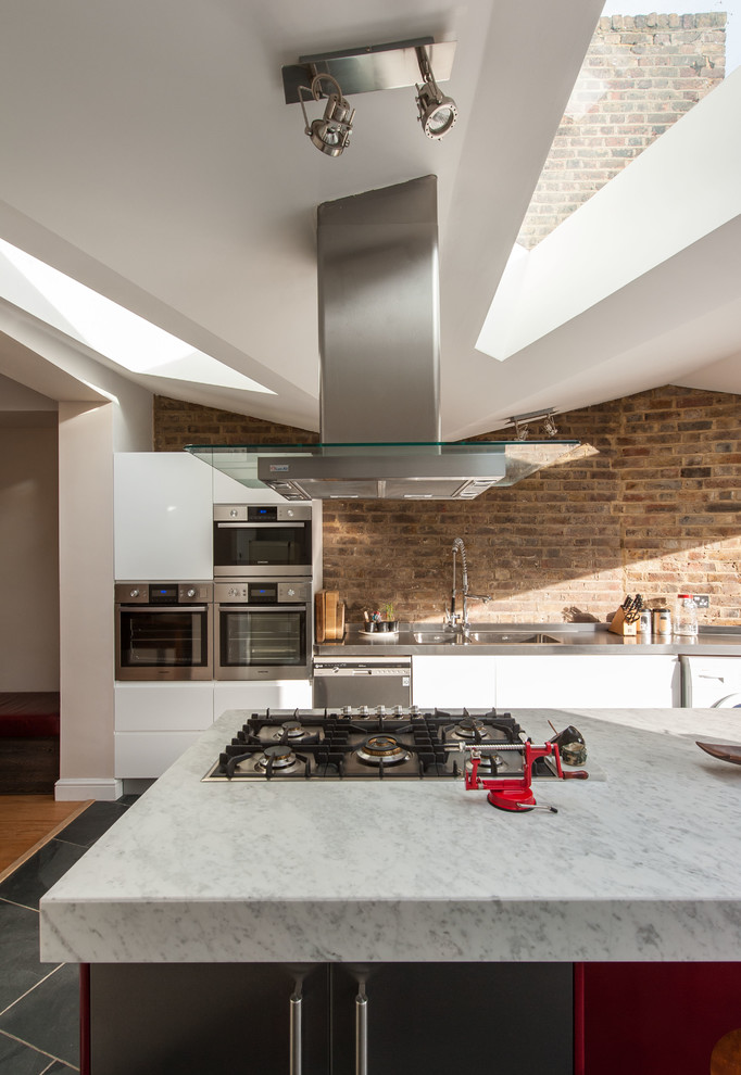 This is an example of a medium sized contemporary single-wall kitchen/diner in London with an integrated sink, flat-panel cabinets, white cabinets, marble worktops, stainless steel appliances, ceramic flooring and an island.